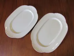 Zwei ovale Servierplatten Zwei weiße ovale Servierplatten mit rosa Dekor auf einem Holztisch