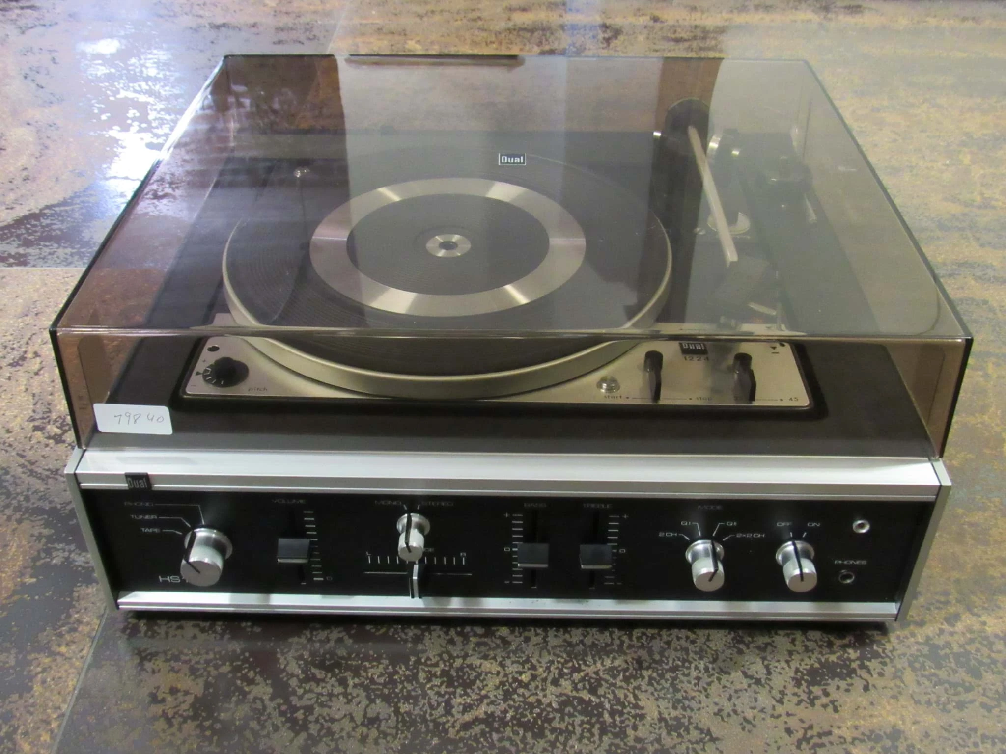 Eine HiFi-Kompaktanlage der Marke Dual mit Plattenspieler unter einer transparenten Abdeckhaube und einem Verstärkerteil mit silbernen Reglern, frontal fotografiert.