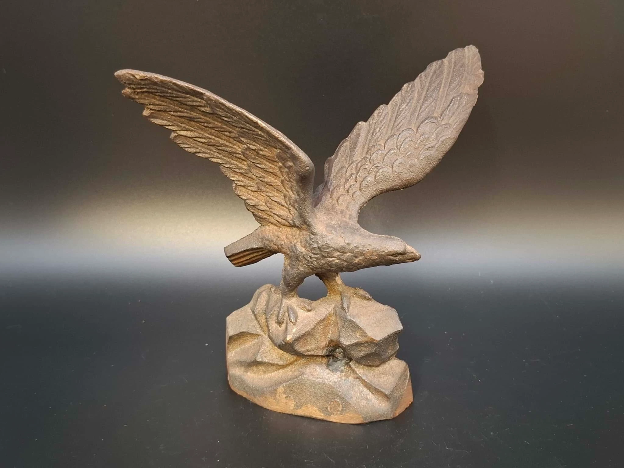 Detaillierte gusseiserne Adlerfigur mit ausgebreiteten Schwingen, die auf einem stilisierten Felsensockel vor dunklem Hintergrund steht