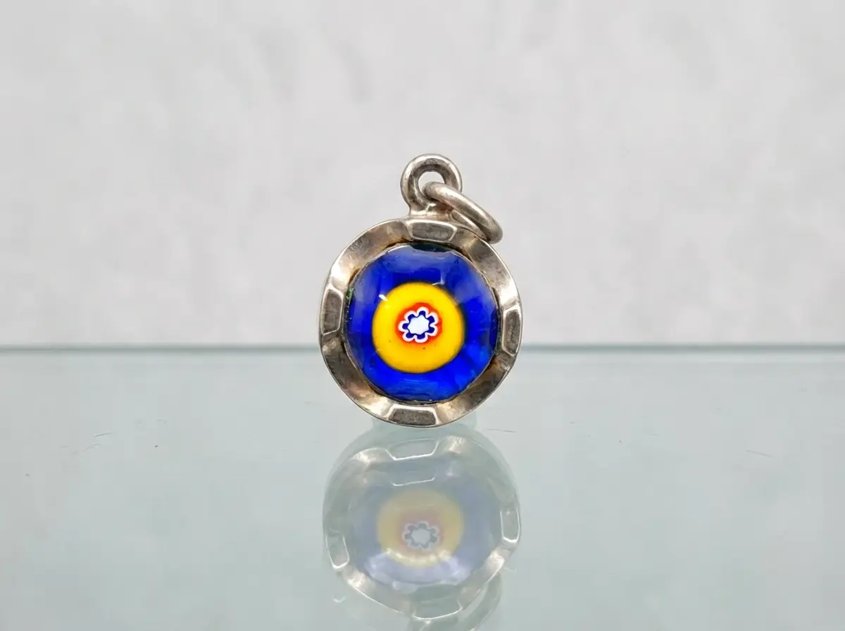 Runder Silberanhänger mit blauem und gelbem Millefiori-Glasmuster auf spiegelndem Untergrund