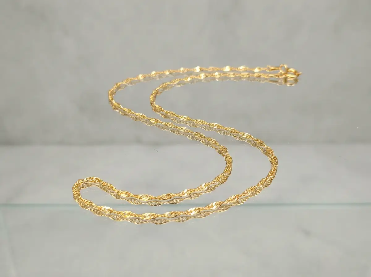 Filigrane goldene Halskette im Singapur-Stil, elegant drapiert auf einer reflektierenden Oberfläche vor hellem Hintergrund