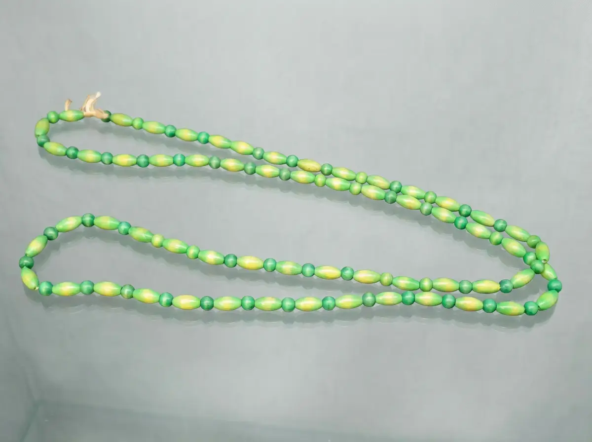 Lange grüne Perlenkette mit abwechselnd runden und ovalen gelb-grünen Elementen auf grauem Untergrund