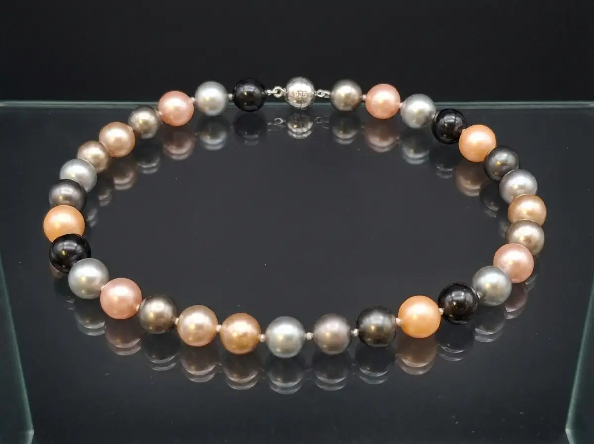 Elegante Multicolor-Perlenkette mit Perlen in Grau, Schwarz und Rosé auf einer spiegelnden schwarzen Glasfläche mit sichtbarem Silberverschluss