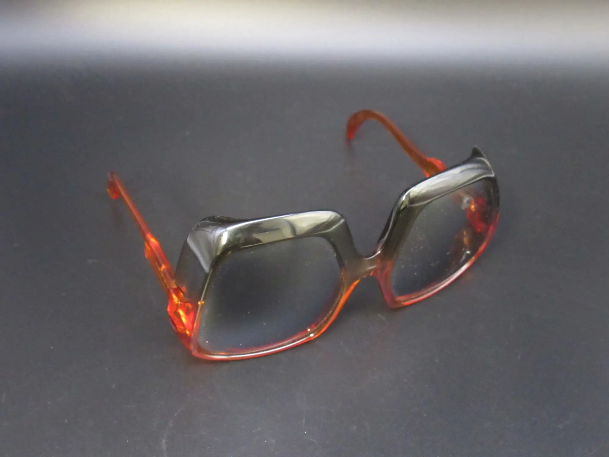 Große Vintage-Brille mit dickem Rahmen und Farbverlauf von Schwarz zu Bernstein vor dunklem Hintergrund