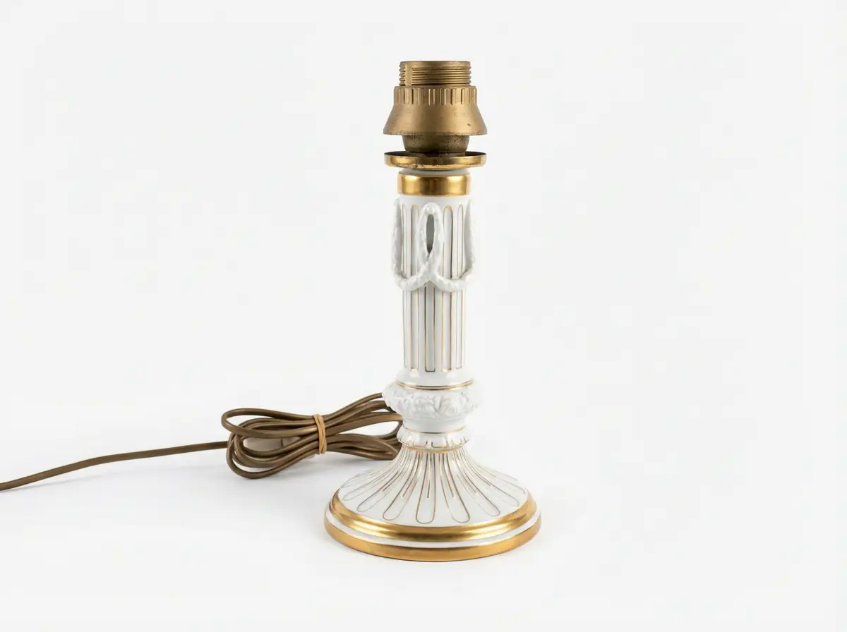 Säulenförmige Tischlampe aus weißem Porzellan mit goldenen Verzierungen und aufgewickeltem braunen Kabel vor weißem Hintergrund