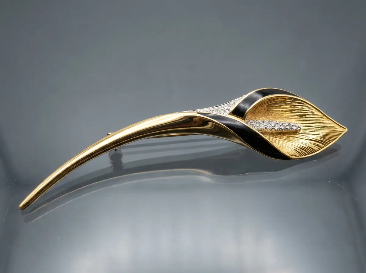 Elegante goldene Brosche in Form einer Calla-Blüte mit schwarzer Emaille und funkelndem Strass-Besatz auf grauem Hintergrund