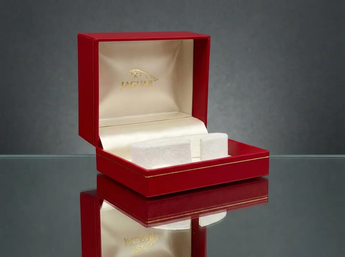Geöffnete rote Jaguar Geschenkbox mit goldenem Logo, cremefarbenem Innenfutter und Polsterung auf einer spiegelnden Glasfläche.