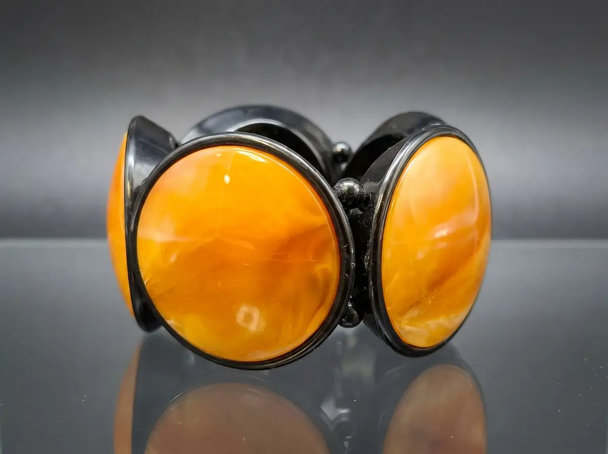 Breites Modeschmuck-Armband mit großen, runden, orange marmorierten Scheiben in schwarzer Fassung auf spiegelndem Untergrund