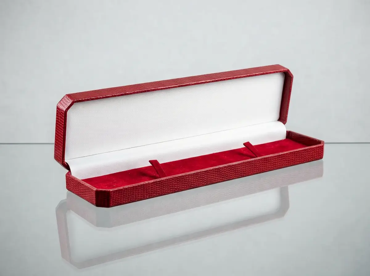 Geöffnete lange rote Schmuckschachtel mit weißem Innenfutter und Halterungen auf spiegelndem Untergrund.