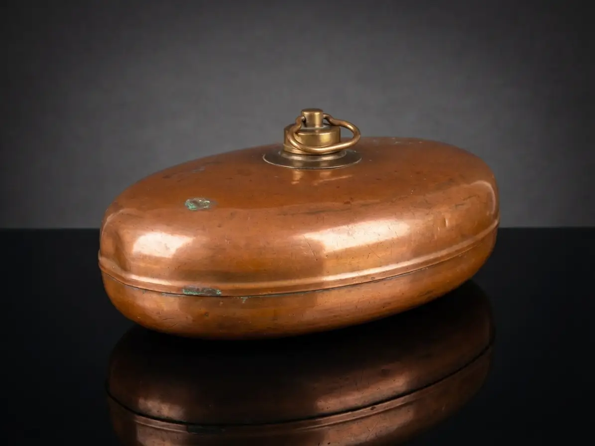 Ovale antike Wärmflasche aus Kupfer mit Messingverschluss und Ringgriff auf spiegelndem schwarzen Untergrund