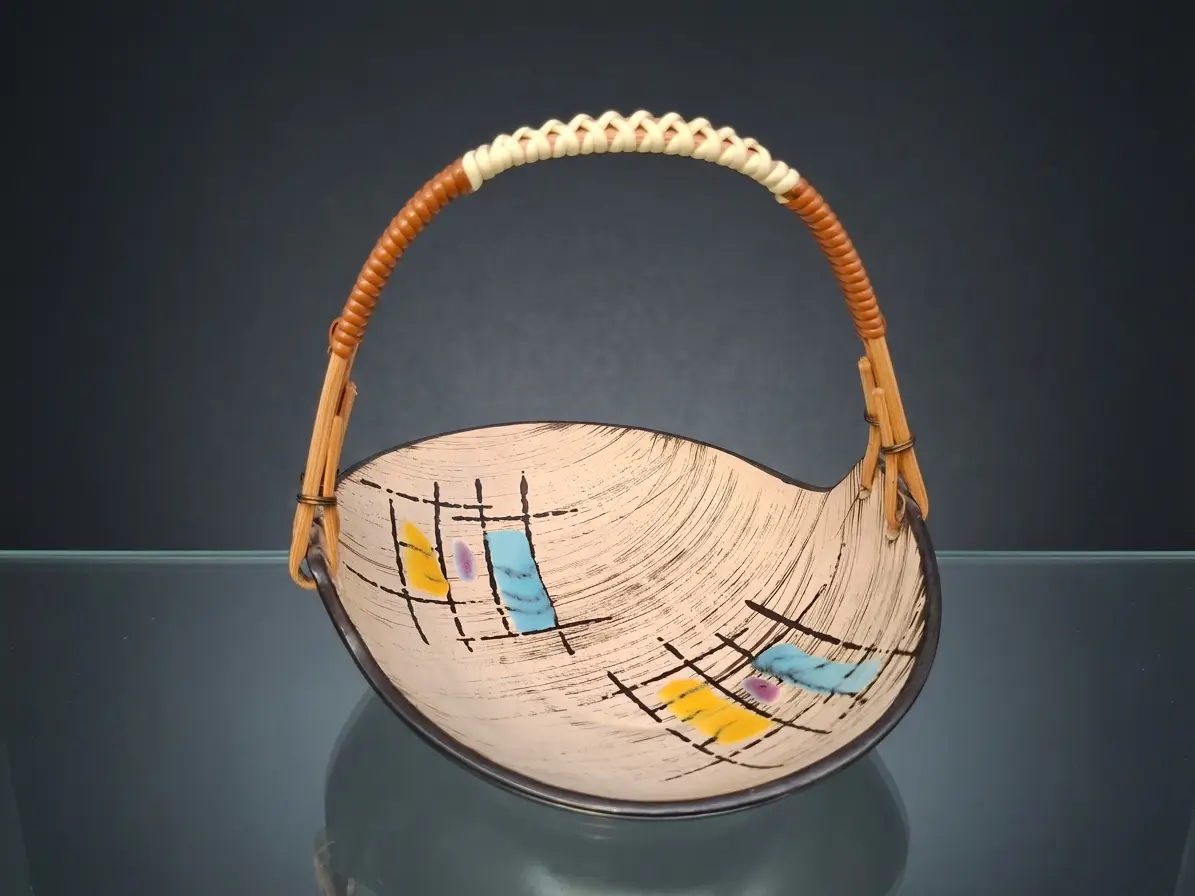 Asymmetrische Keramikschale mit geflochtenem Henkel und abstraktem Dekor in Gelb, Blau und Schwarz auf dunklem Hintergrund