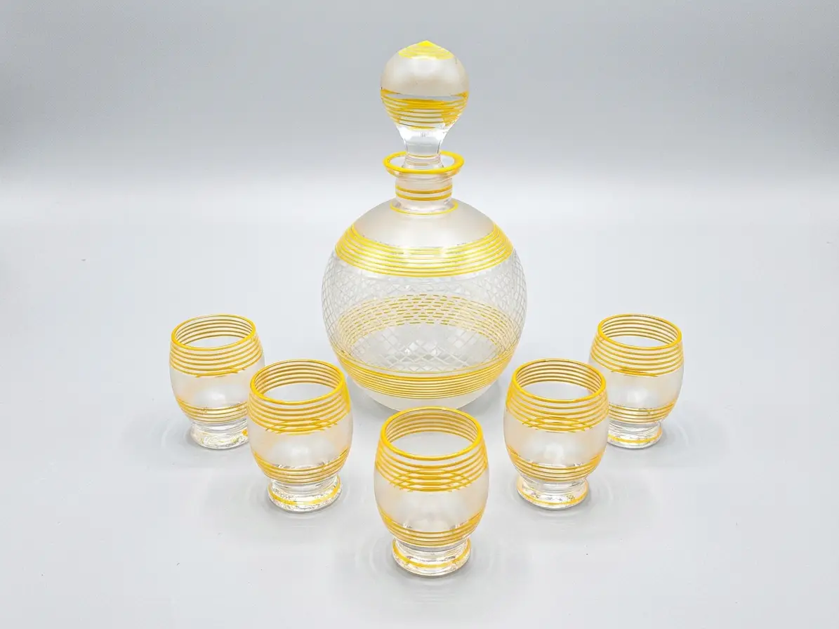 Vintage Likör-Set bestehend aus einer bauchigen Karaffe mit Stopfen und fünf Schnapsgläsern, verziert mit gelben Streifen und mattiertem Glas vor grauem Hintergrund.