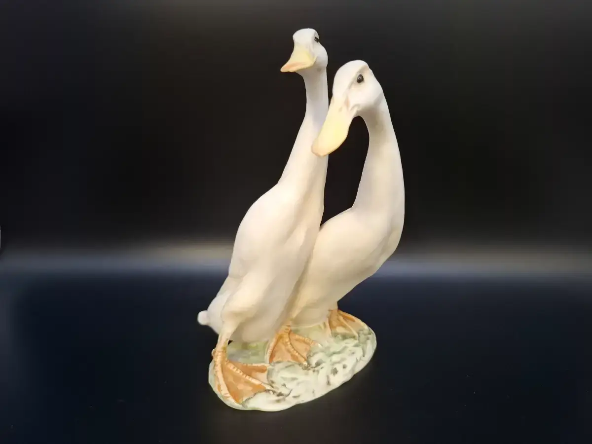 Zwei weiße Enten als dekorative Porzellanfigur vor einem schwarzen Hintergrund.
