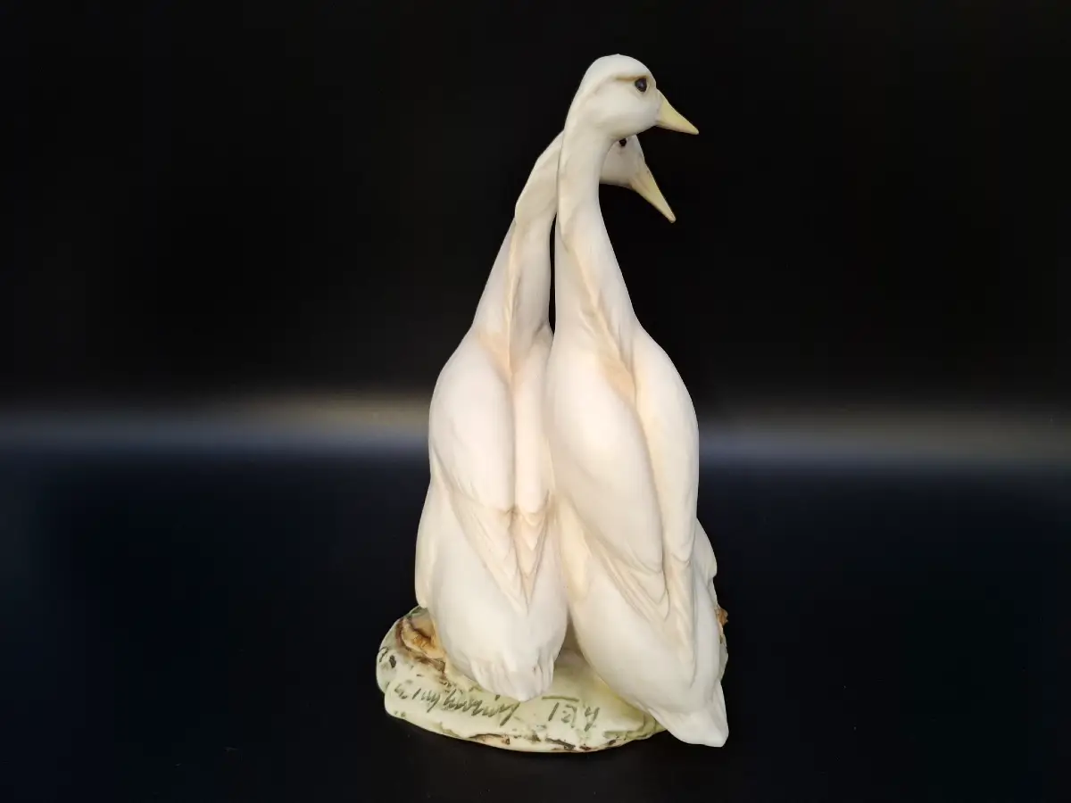 Vintage Porzellanfigur von zwei weißen Enten auf einem Natursockel vor schwarzem Hintergrund