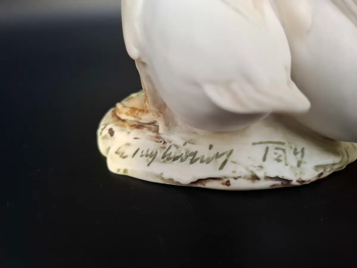 Nahaufnahme des Sockels einer weißen Porzellanfigur mit der Künstlersignatur G. Tagliariol Tay.